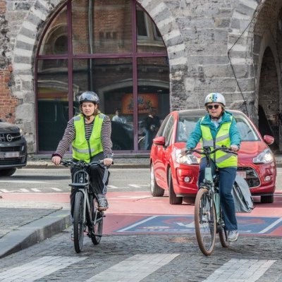 2 fietsers naast elkaar in een fietszone, auto die achter hen rijdt